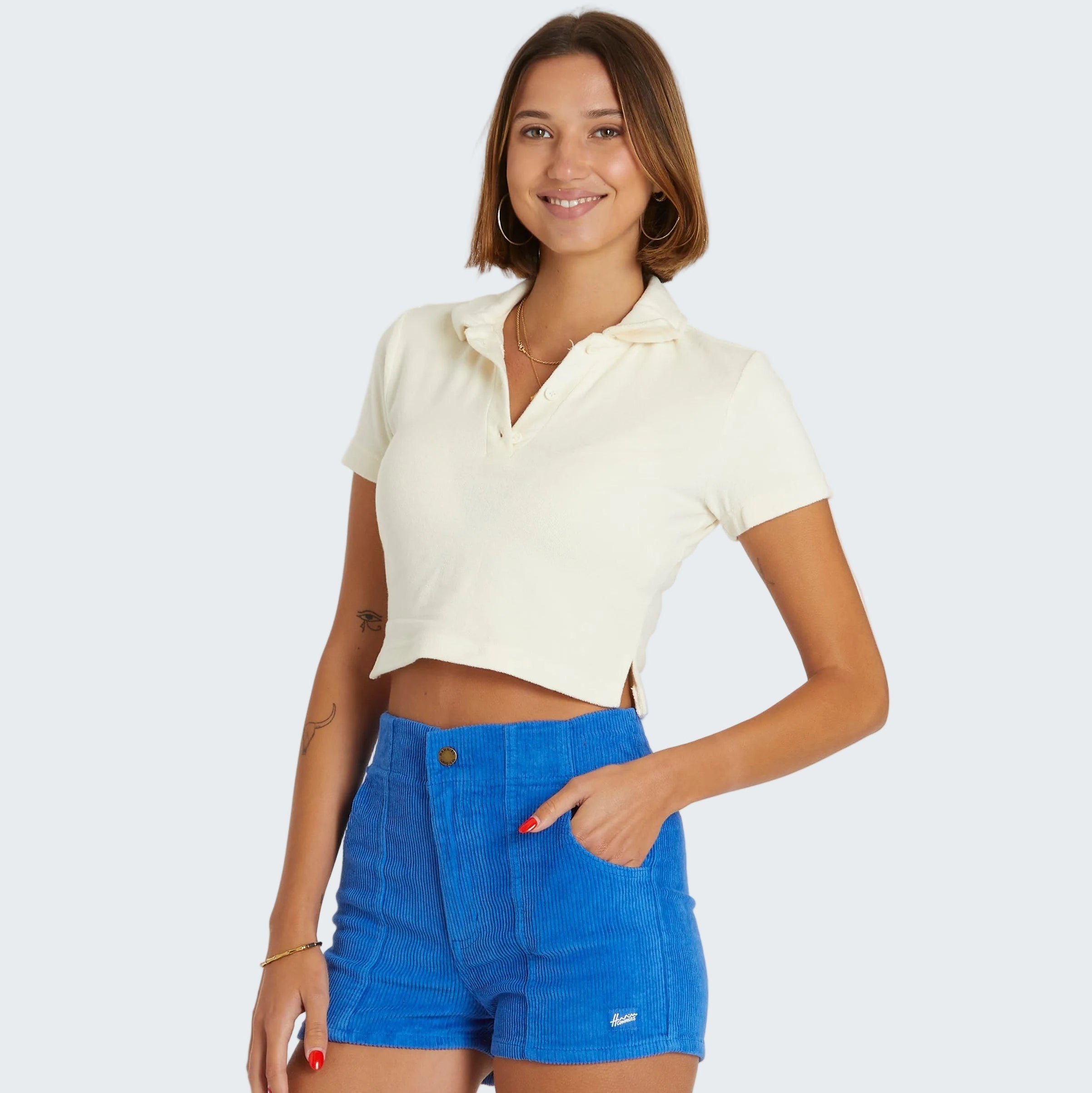 Woman wearing a white cropped top and blue shorts on a white background