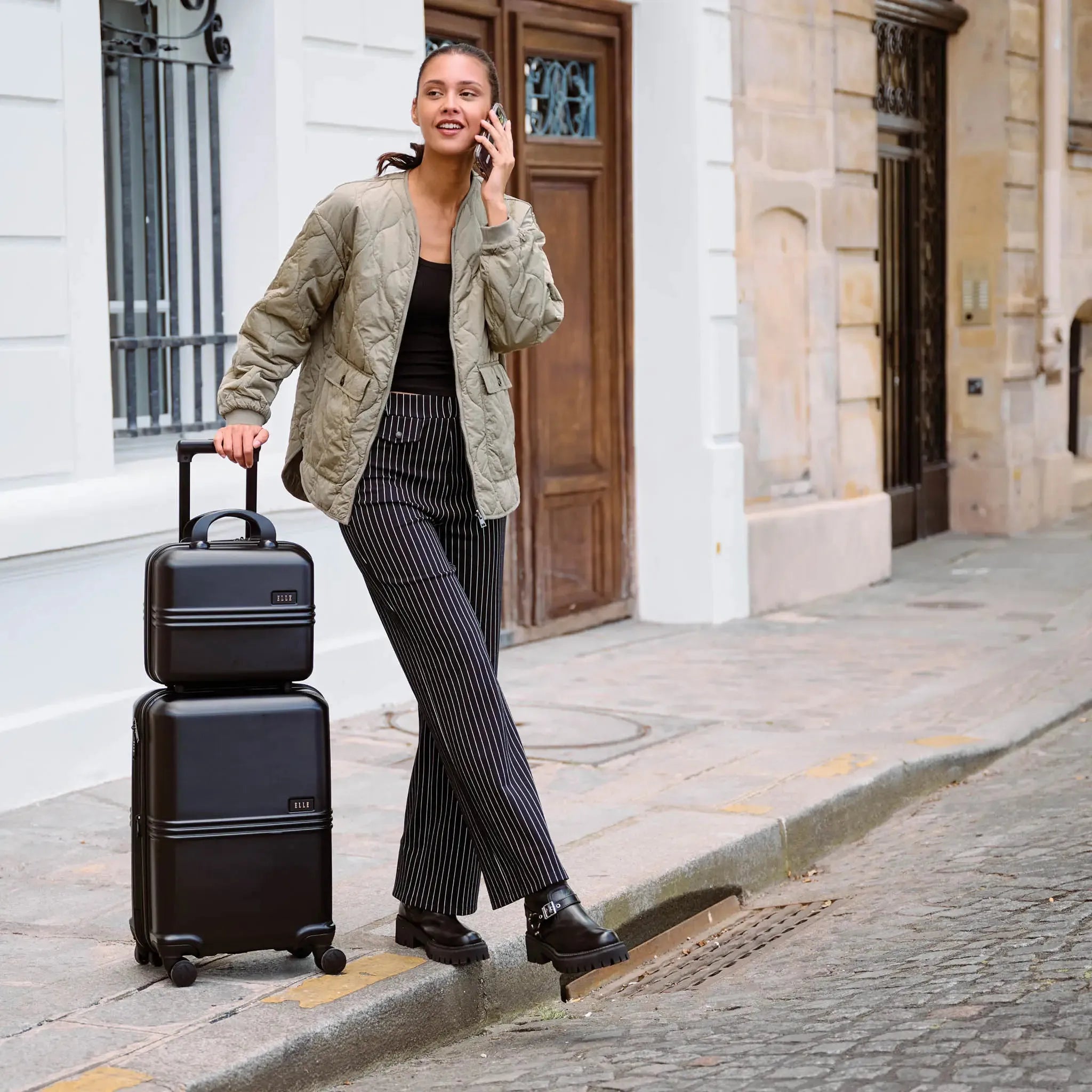 Woman with black ELLE spinner luggage set — vacation wear essentials for beach trips and city adventures at Sun of the Beach Boutique