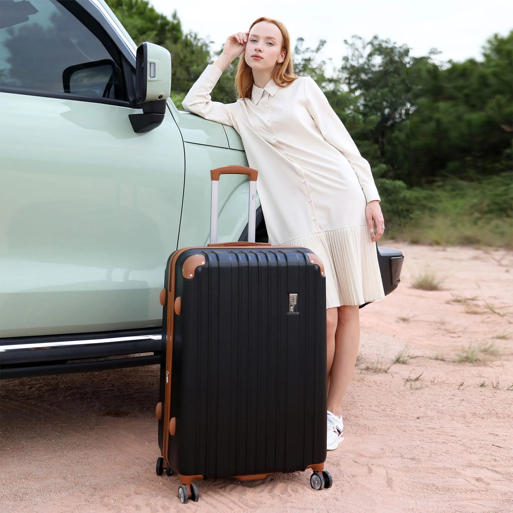Woman standing next to a black suitcase near a car on a dirt road.