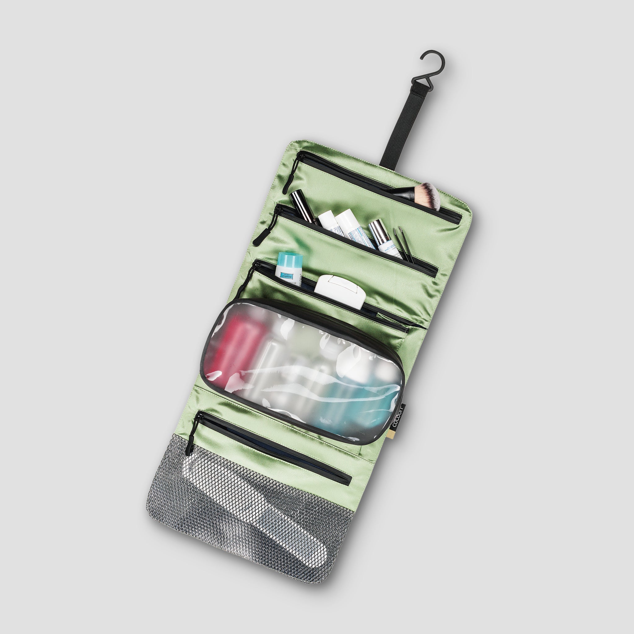 Green travel toiletry bag with black zippers on a light gray background
