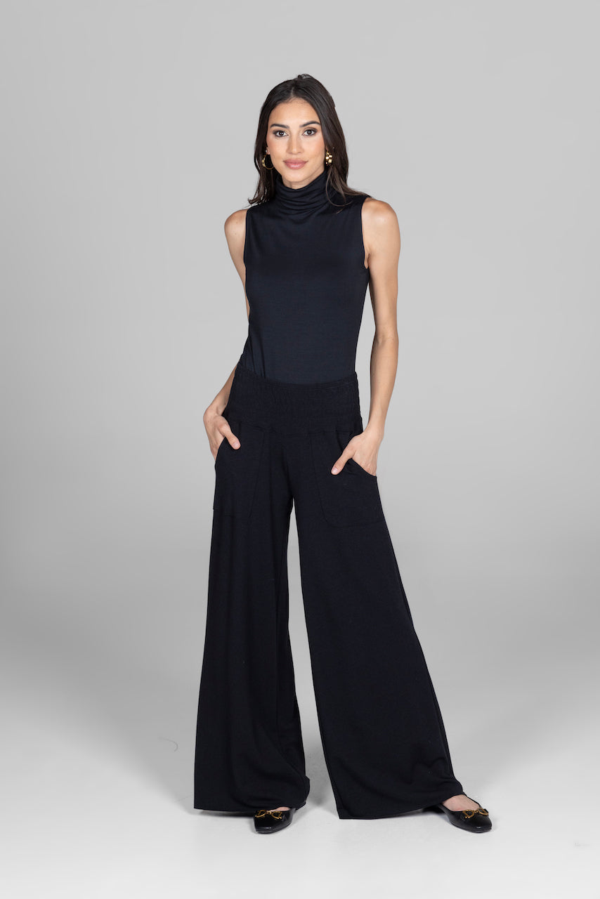 Woman wearing a black sleeveless top and wide-leg pants on a gray background