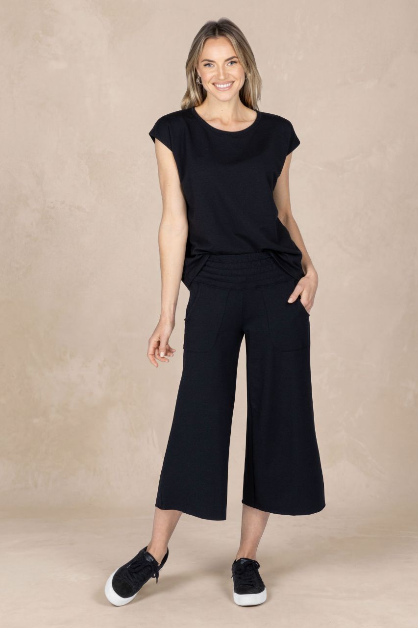 Woman wearing a black outfit with wide-leg pants on a beige background