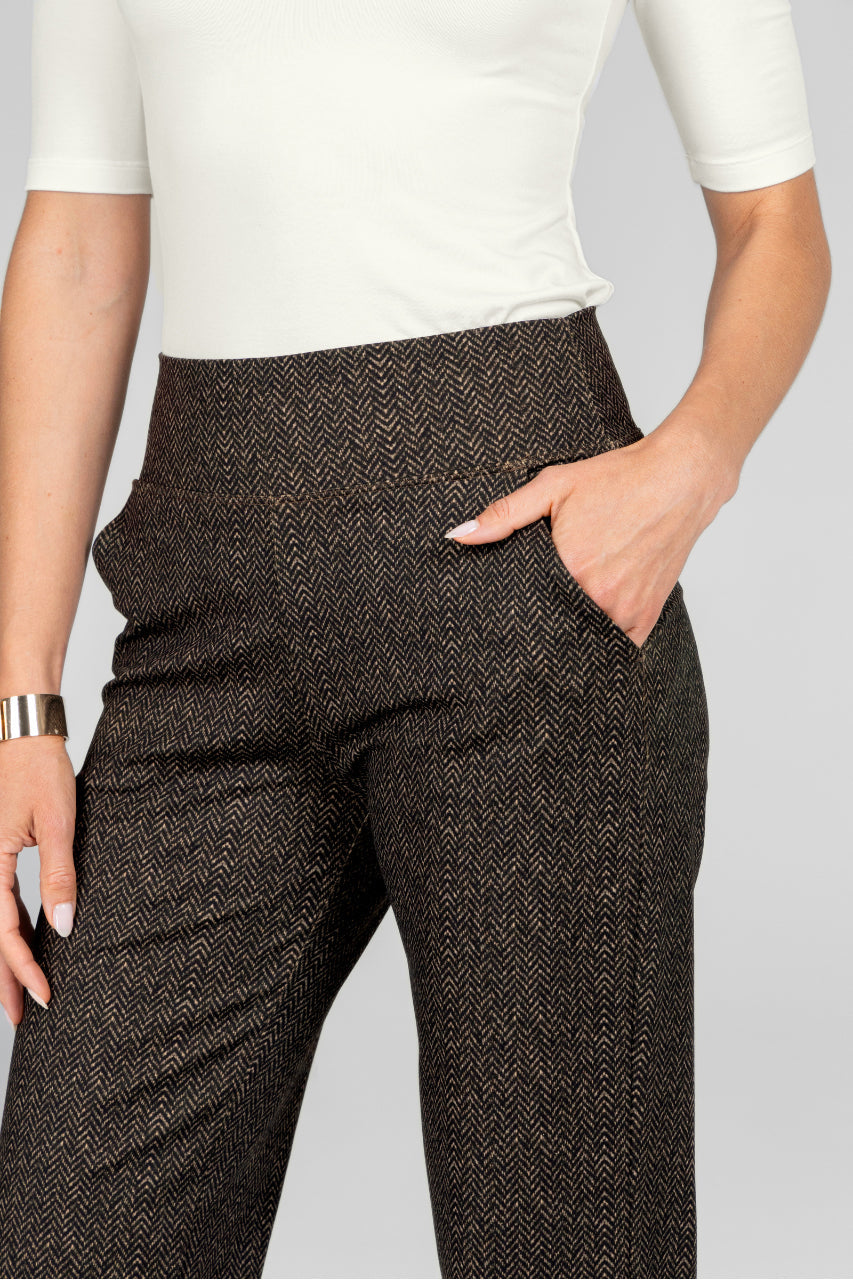 Person wearing brown herringbone pants with a white top on a light gray background