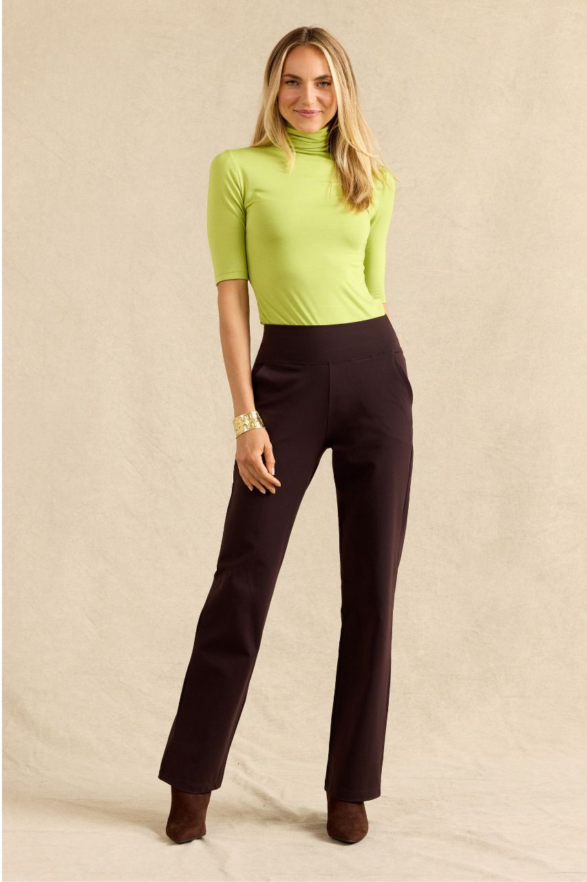 A woman modeling a lime green short-sleeve mock neck top and dark brown straight-leg trousers against a neutral beige backdrop.