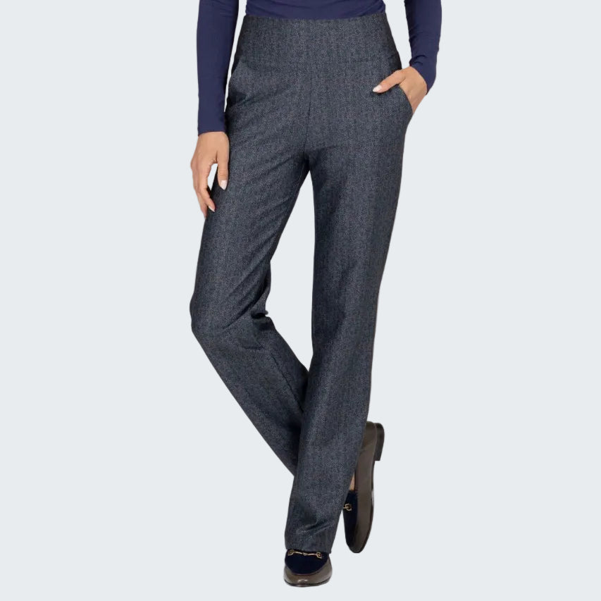 A person wearing high-waisted, straight-leg charcoal gray trousers with a subtle houndstooth pattern, paired with a navy blue long-sleeve top and dark loafers, standing against a textured beige backdrop.