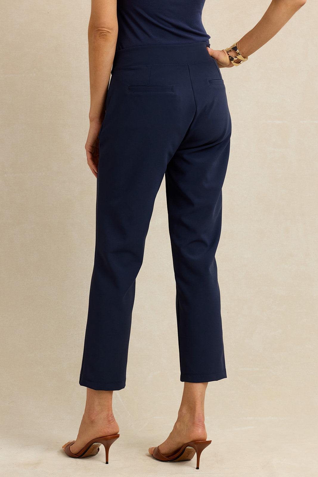A model shown from the back wearing navy blue cropped trousers, a matching navy top, and brown heeled mule sandals against a neutral beige studio background.