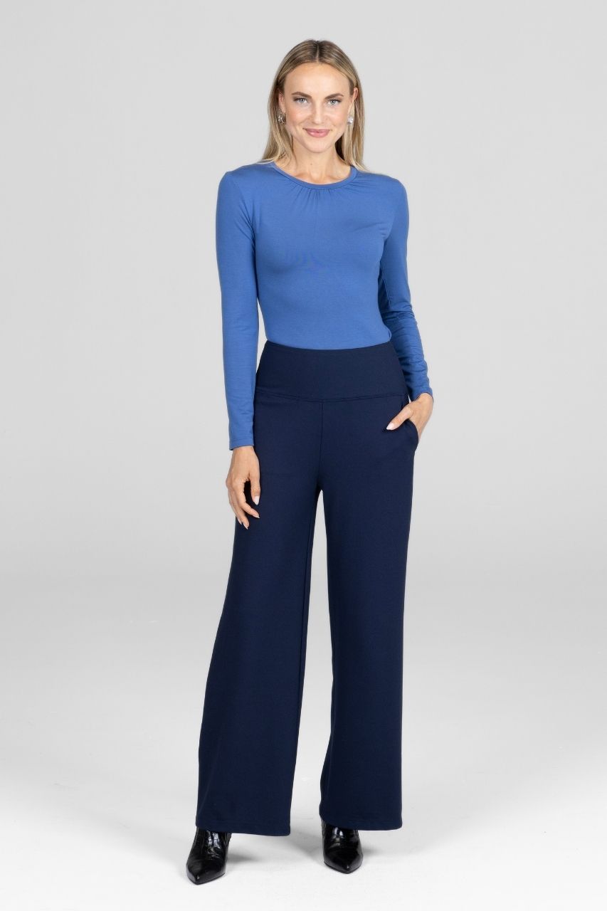 Woman wearing a blue long-sleeve top and navy pants on a white background