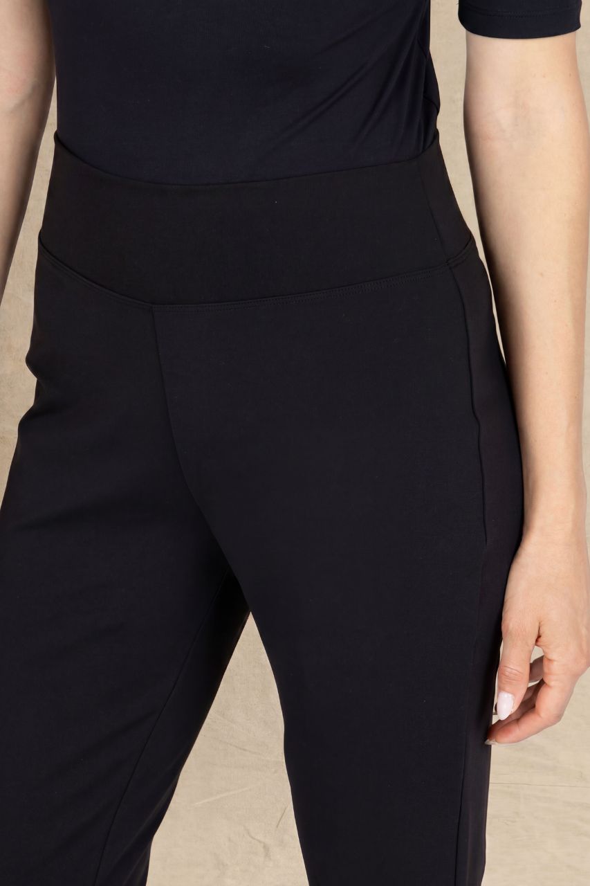 Close-up of a person wearing black high-waisted pants with a wide waistband and side seam detailing, paired with a dark navy top against a light beige background.