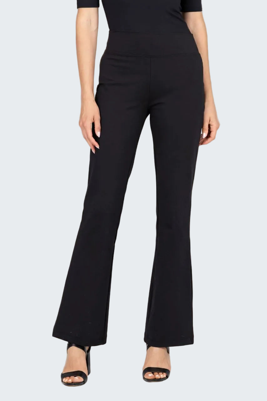 A model wearing black high-waisted flare pants with a smooth texture, paired with black sandals, against a neutral beige textured backdrop.