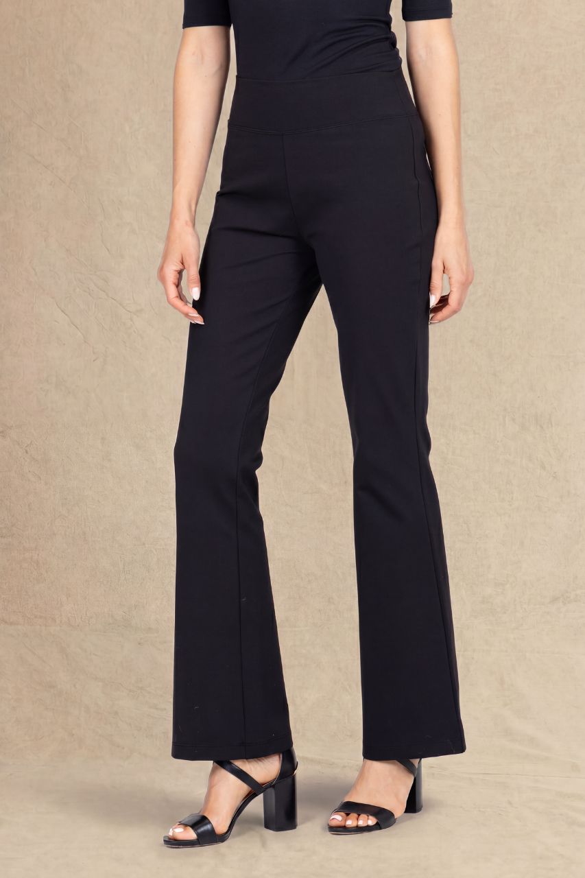 A model wearing black high-waisted, wide-leg trousers and black strappy block-heel sandals, standing against a textured beige studio backdrop.