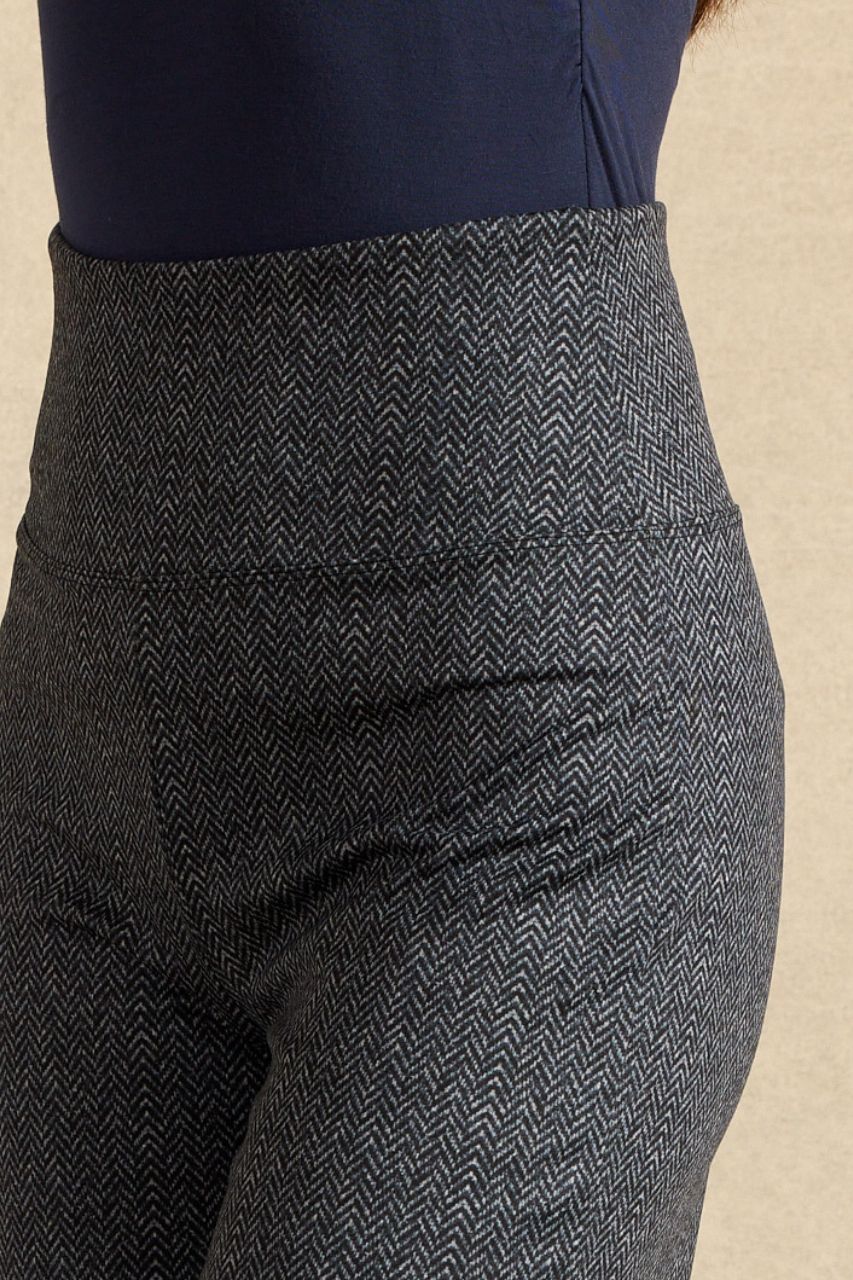 Close-up of a person wearing high-waisted herringbone patterned leggings in dark gray and black, paired with a navy top, against a neutral beige background.