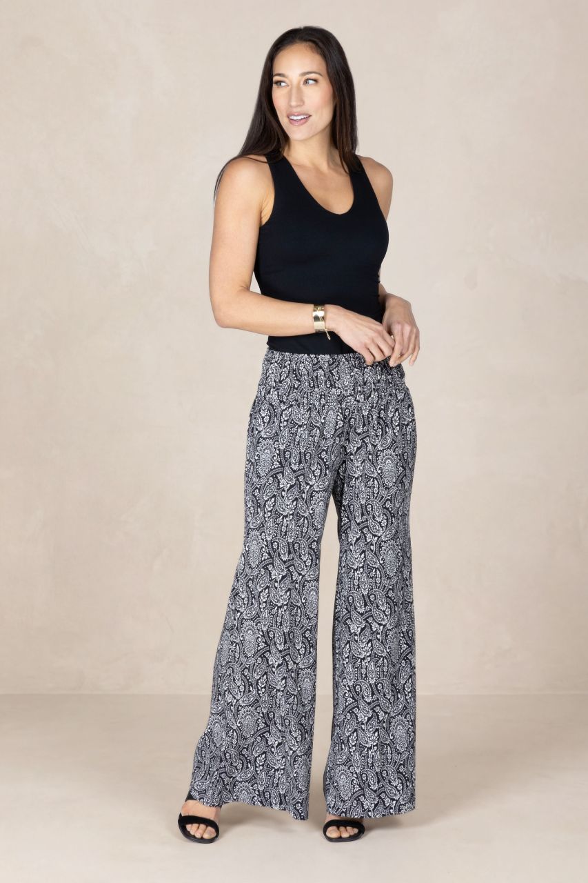 Woman wearing a black tank top and patterned pants on a beige background