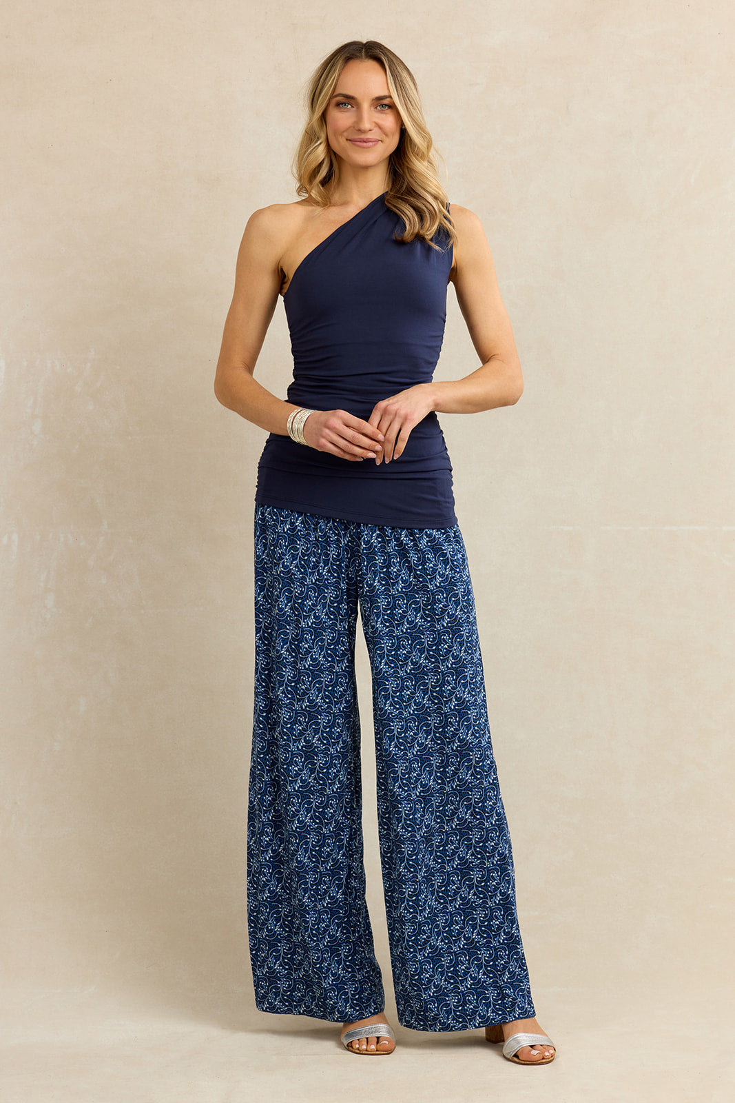 Woman wearing a navy one-shoulder top and blue patterned pants against a beige background