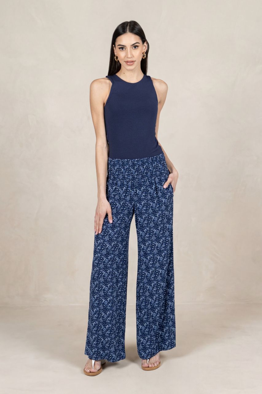 Woman wearing a navy sleeveless top and blue patterned pants on a beige background