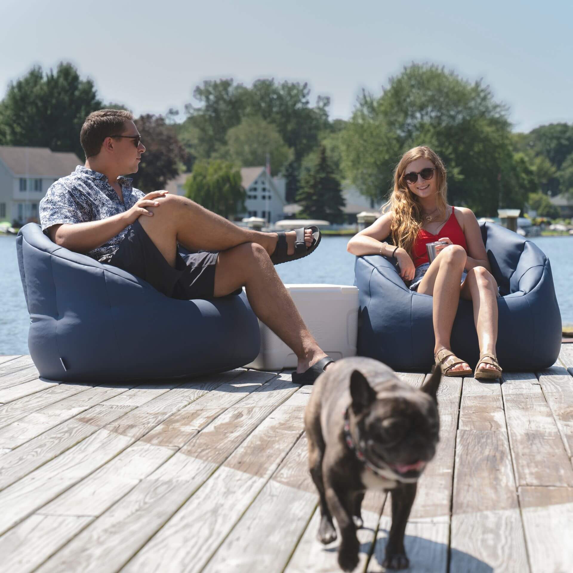 Two people sitting on bean bags by a lake with a dog in the foreground.