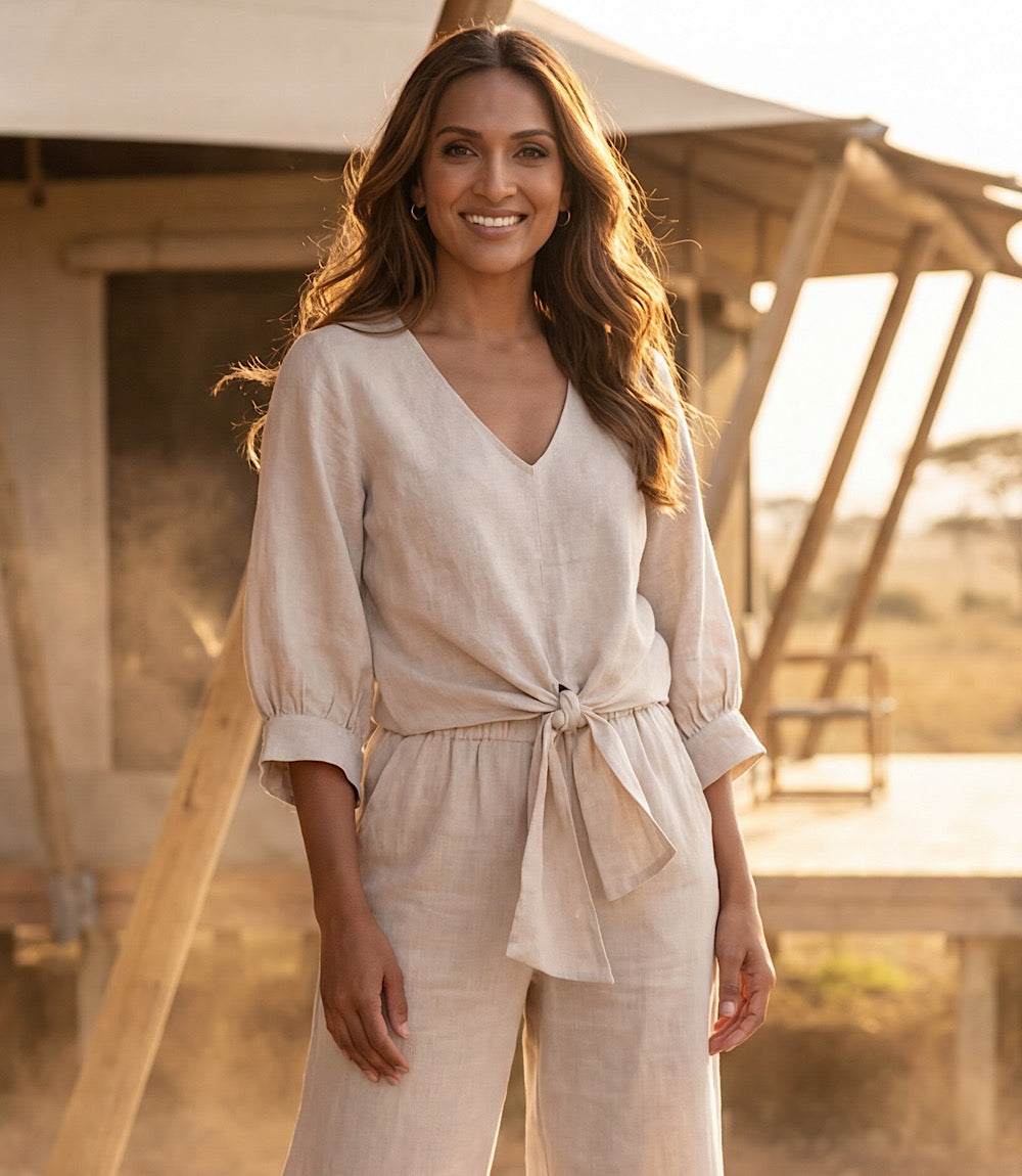 Woman in a beige outfit standing in front of a wooden structure with a warm glow.
