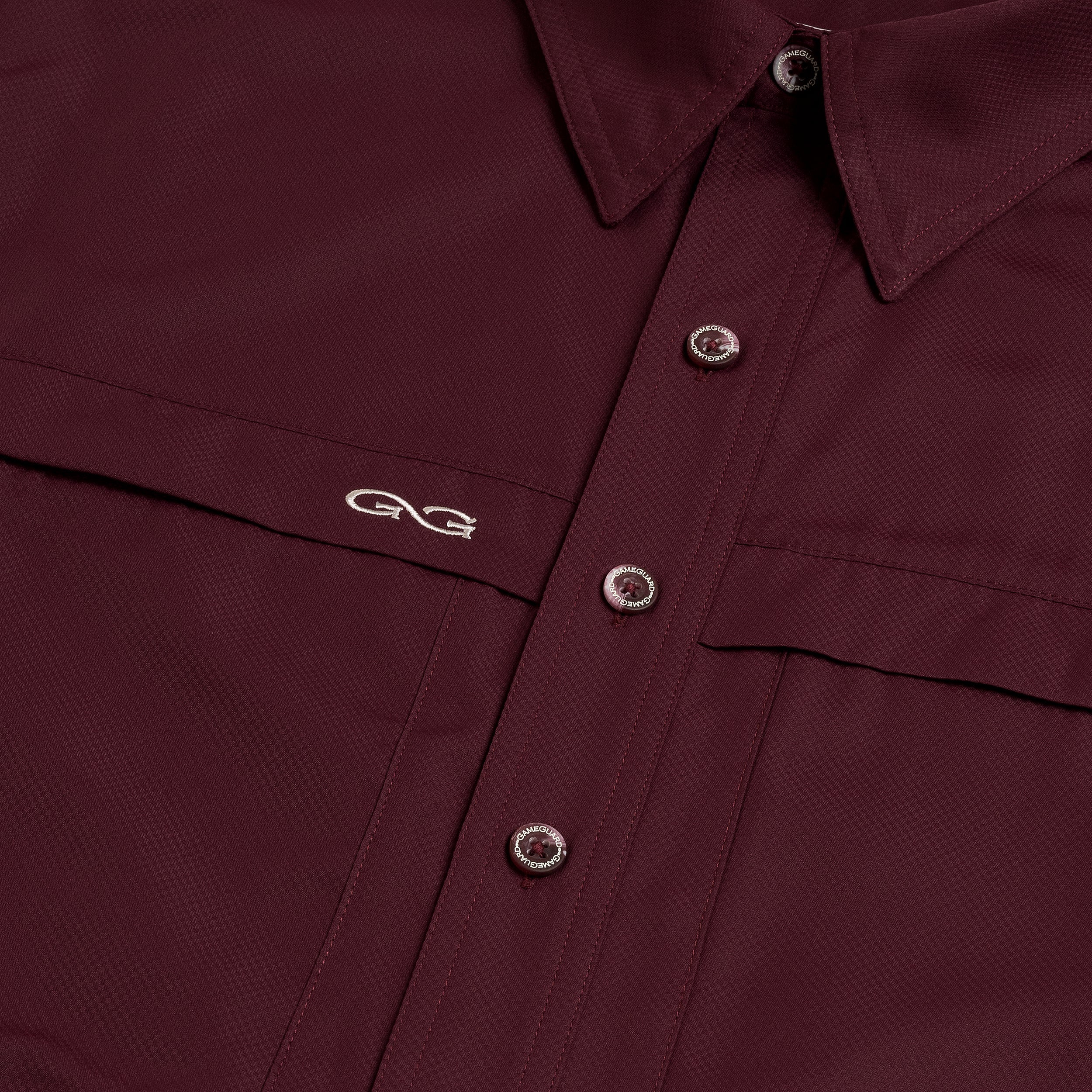 Close-up of a burgundy shirt with button details and a logo on the chest.