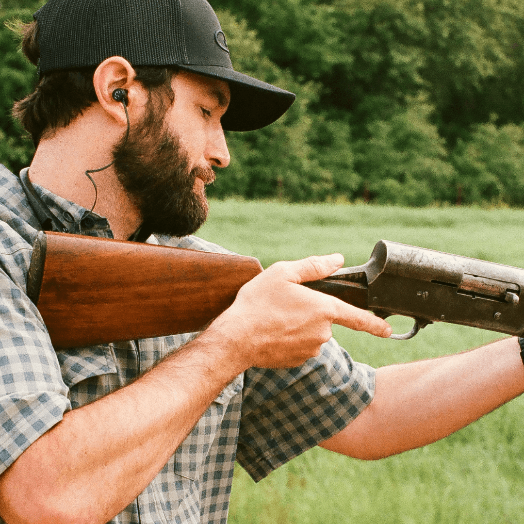 Man holding a rifle in a field with greenery in the background