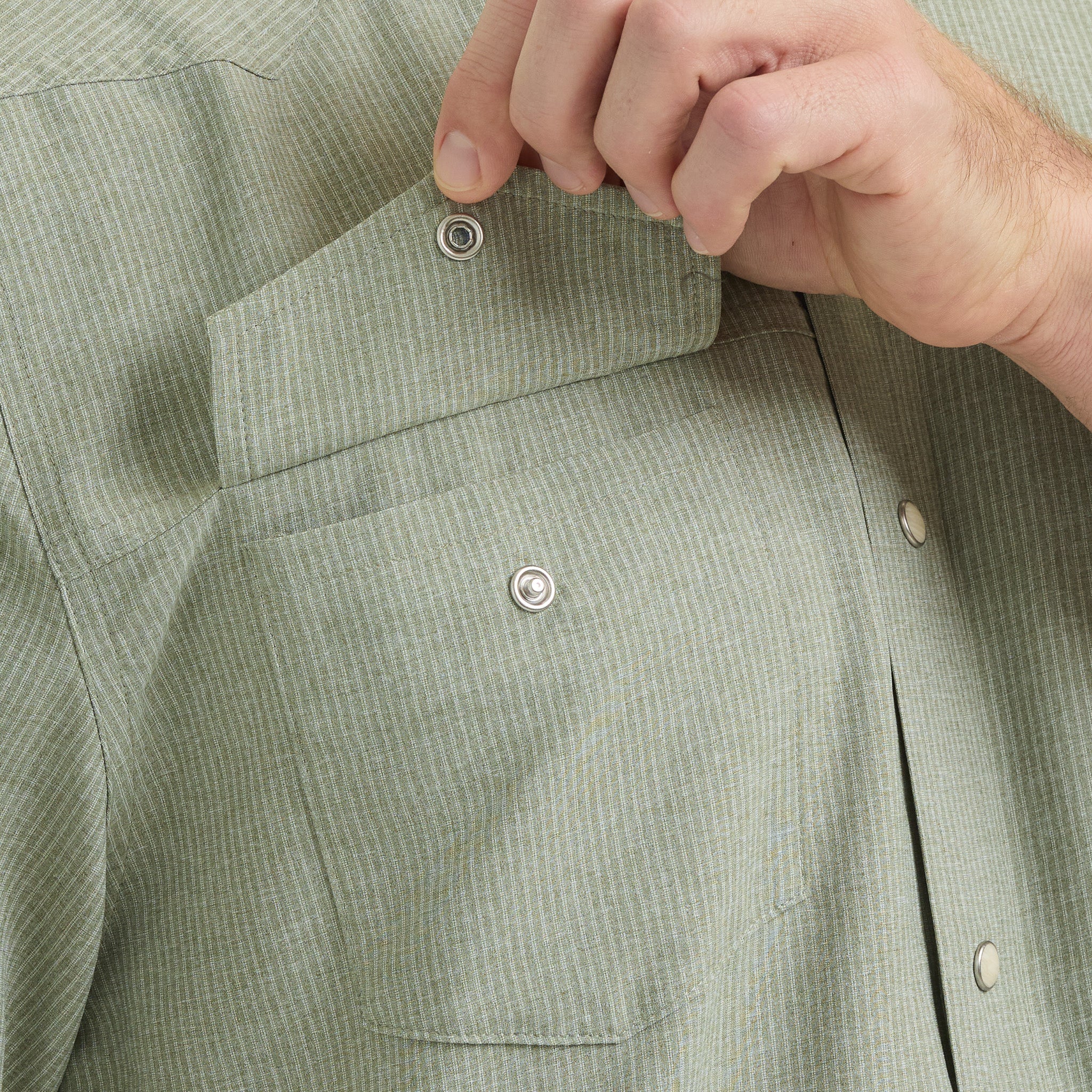 Close-up of a person buttoning a light green shirt with a textured pattern.
