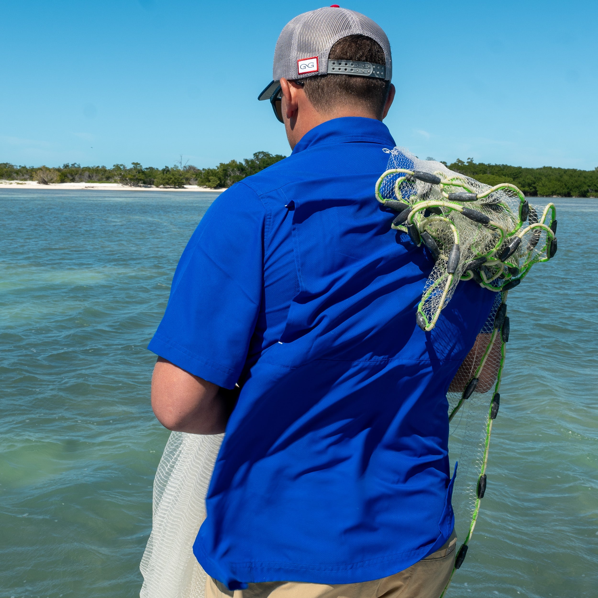 Man in blue shirt and cap with fishing gear by a body of water