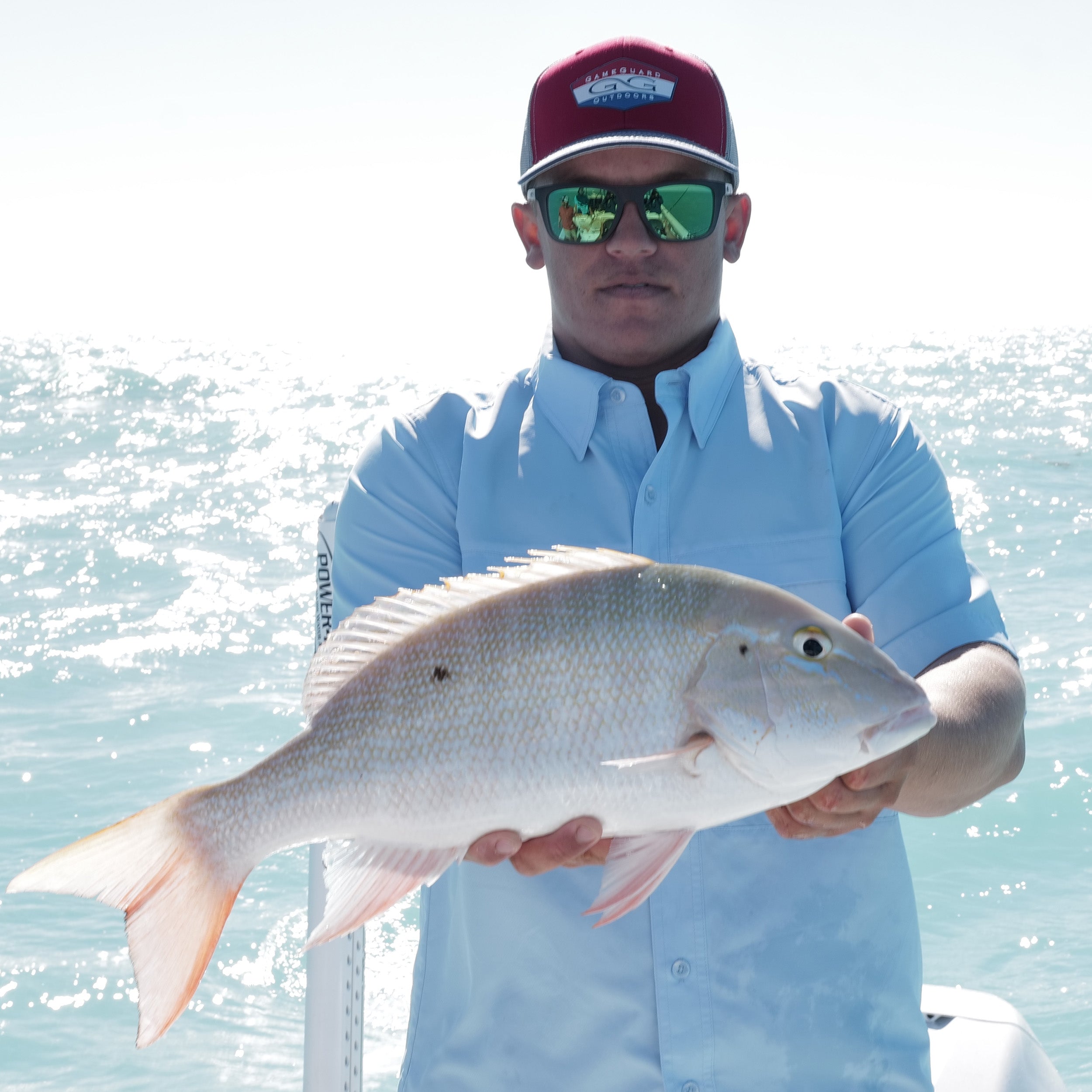 Man holding a large fish on a boat with water in the background