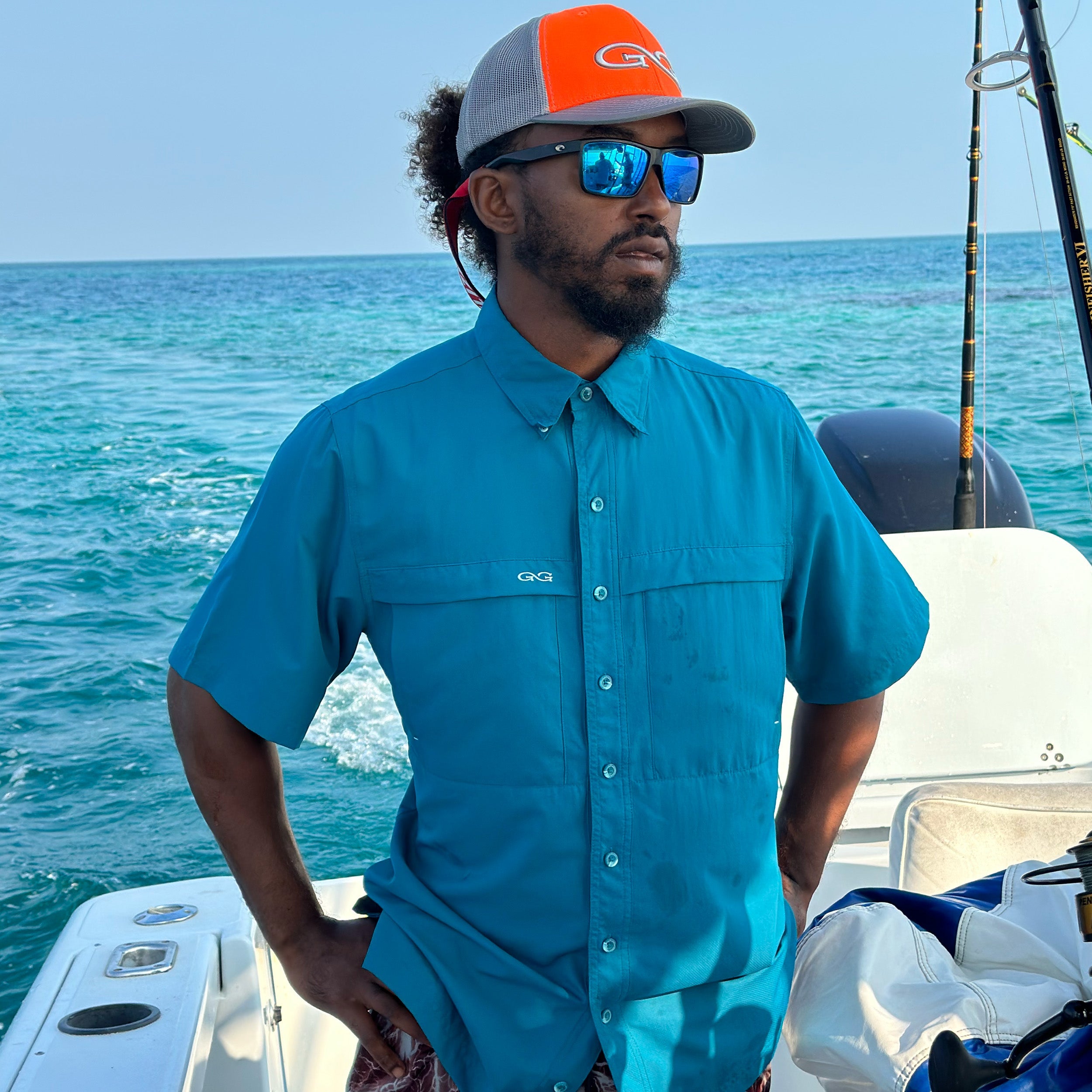 Man on a boat wearing a blue shirt and orange cap with ocean in the background