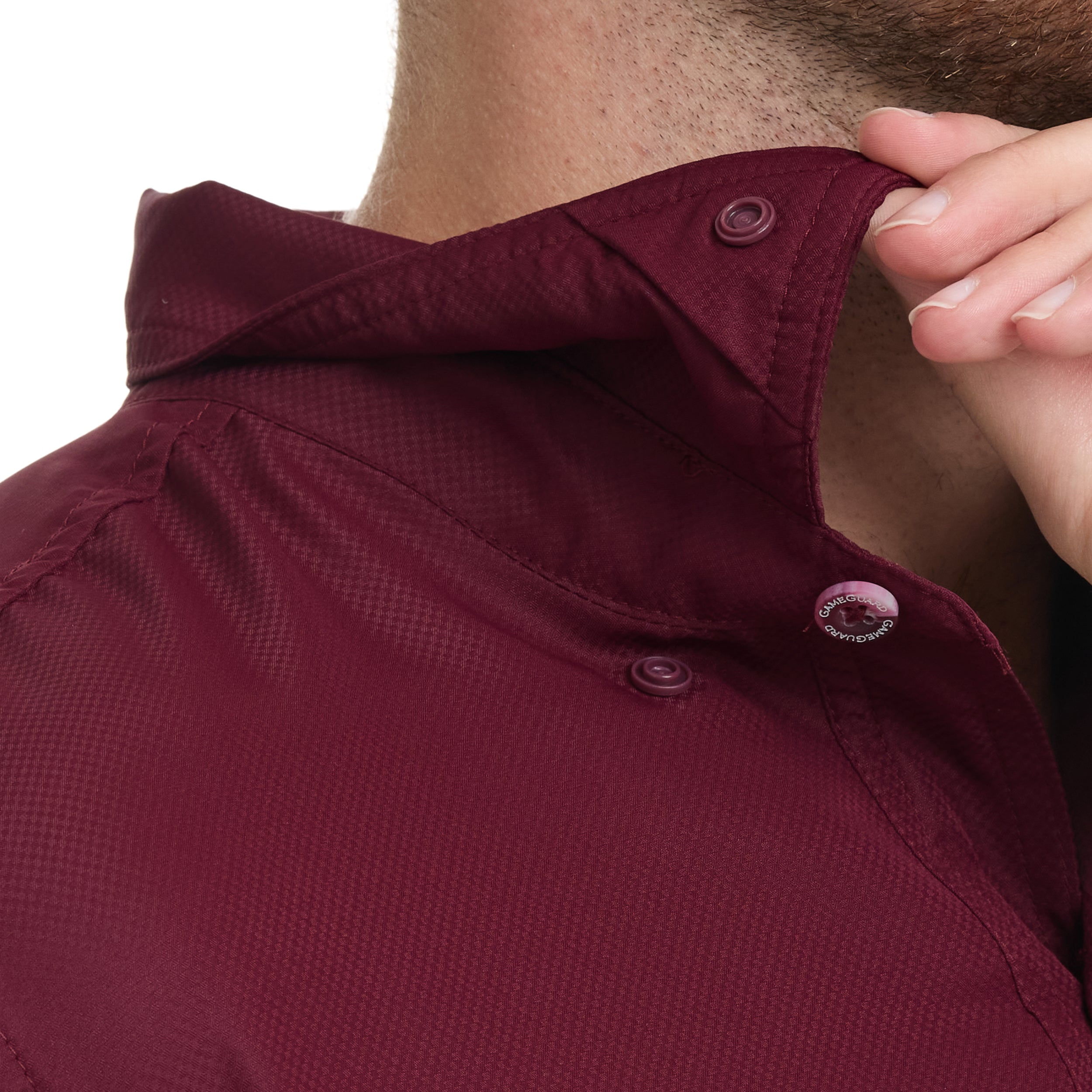 Close-up of a maroon shirt with a hand adjusting the collar on a white background