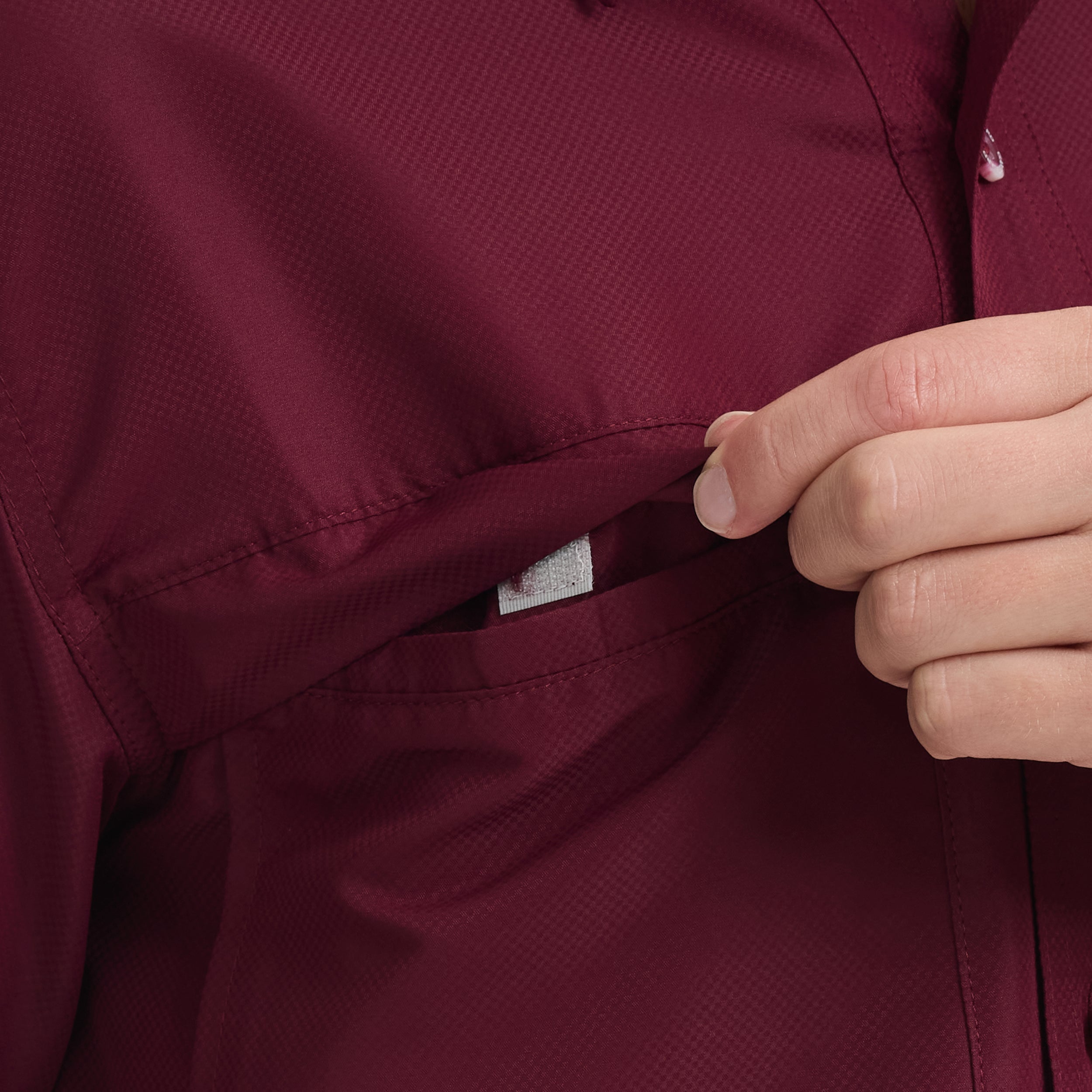 Close-up of a hand buttoning a burgundy shirt