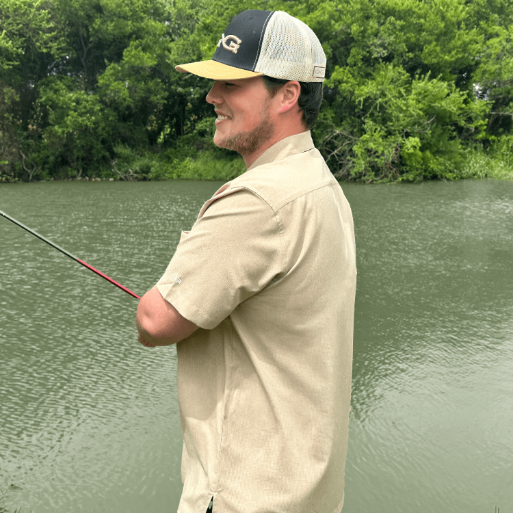 Man fishing by a body of water with greenery in the background