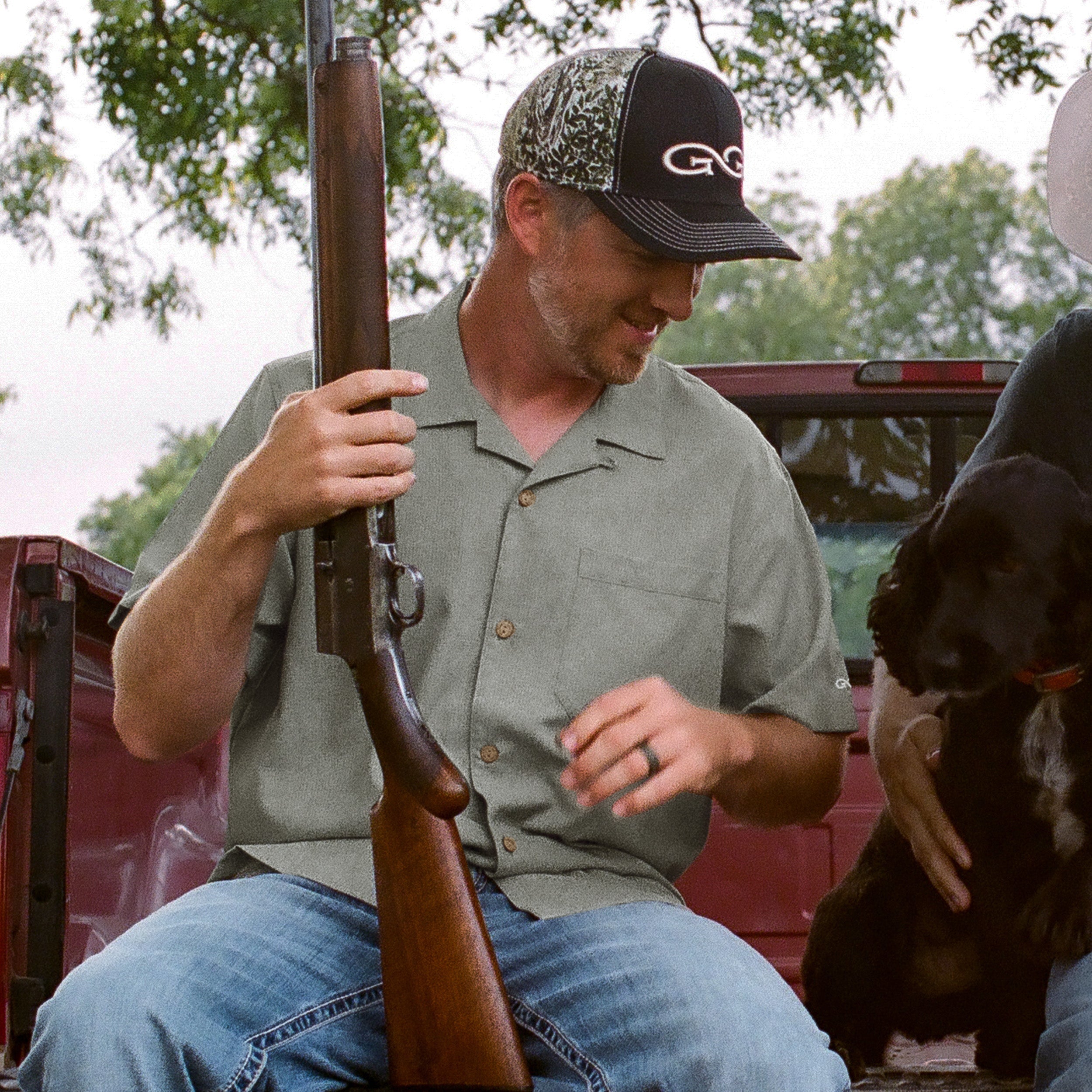 Man holding a rifle with a dog sitting next to him, outdoors.
