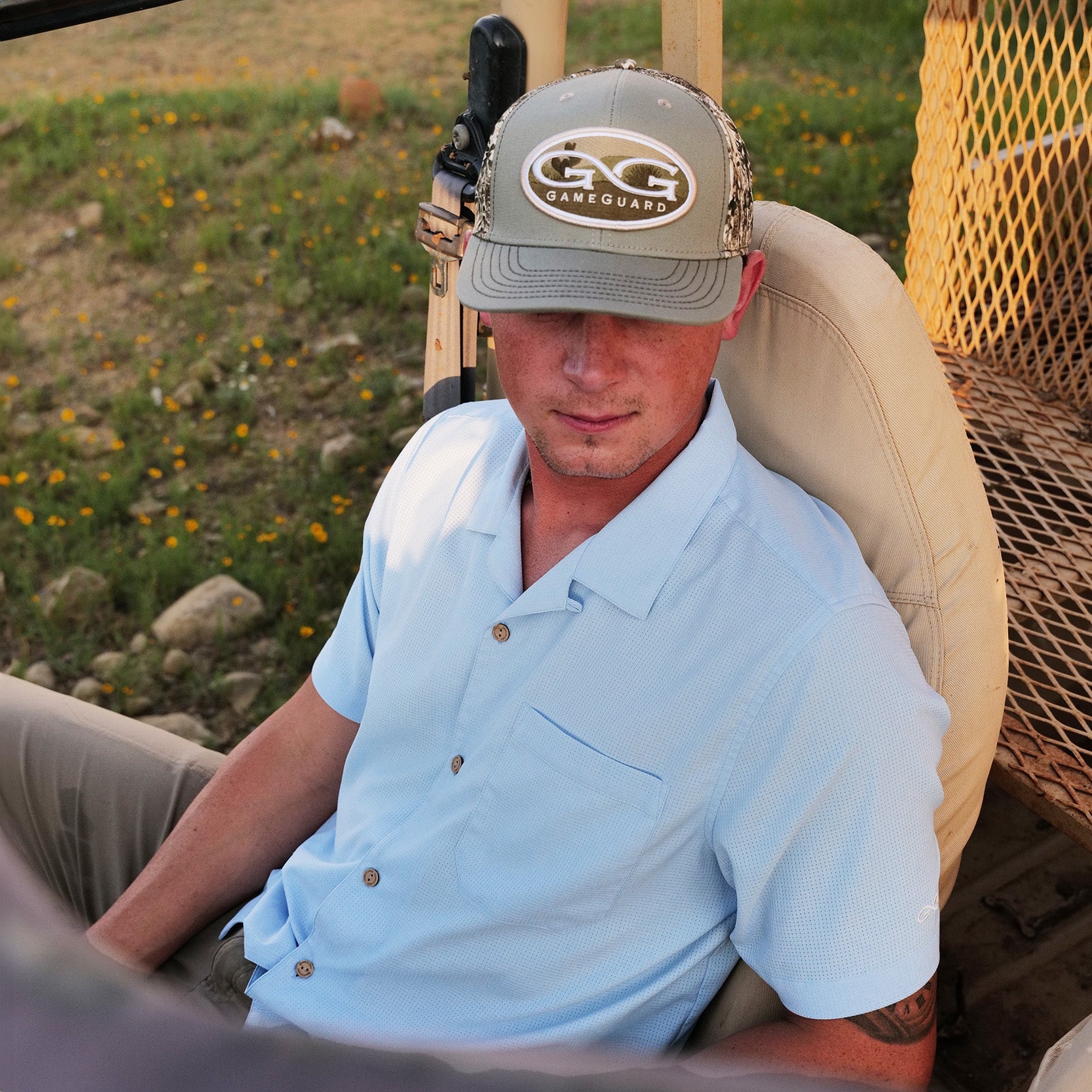 Man wearing a cap with 'GG GameGuard' logo, sitting in a vehicle outdoors.