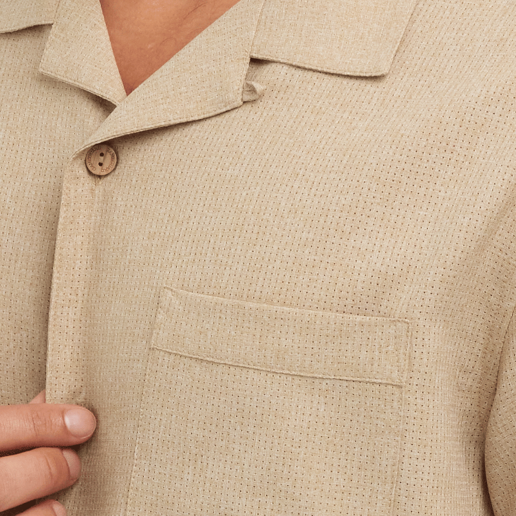 Close-up of a beige textured shirt with a button and pocket.