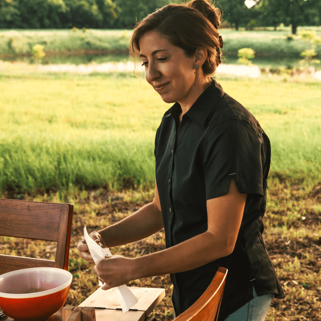 Woman standing outdoors in a field, holding a piece of paper.