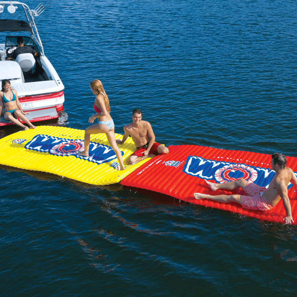 People on inflatable water mats with a boat in the background on a body of water.