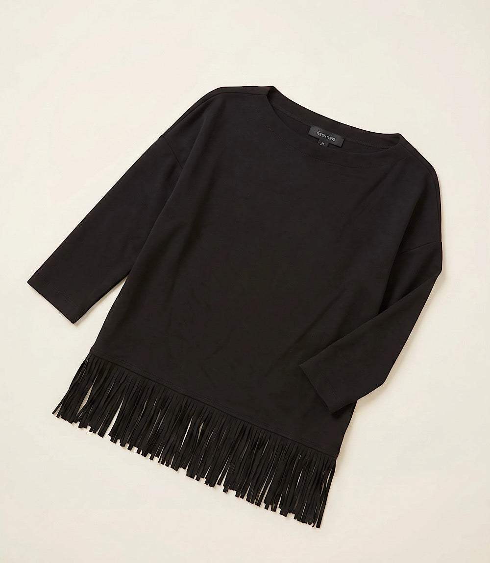 A black long-sleeve knit top with fringe trim along the hem, laid flat on a light beige background.