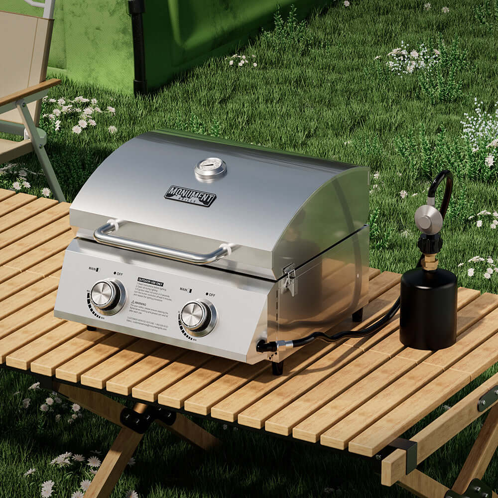 Stainless steel grill on a wooden table outdoors with grass and flowers in the background
