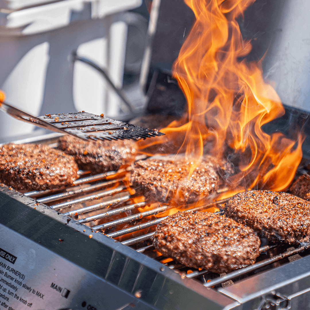 Hamburgers cooking on a grill with flames