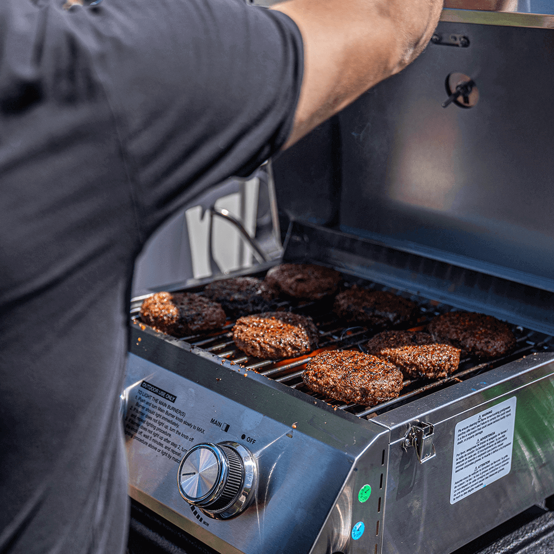Person grilling hamburgers on a portable grill outdoors