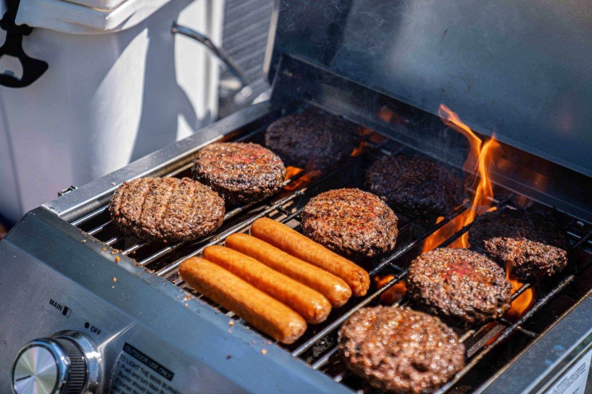 Hot dogs and hamburgers cooking on a grill with flames.