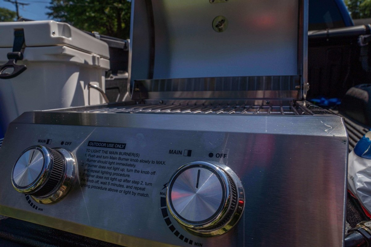 Close-up of a gas grill with control knobs and brand name on a sunny day.