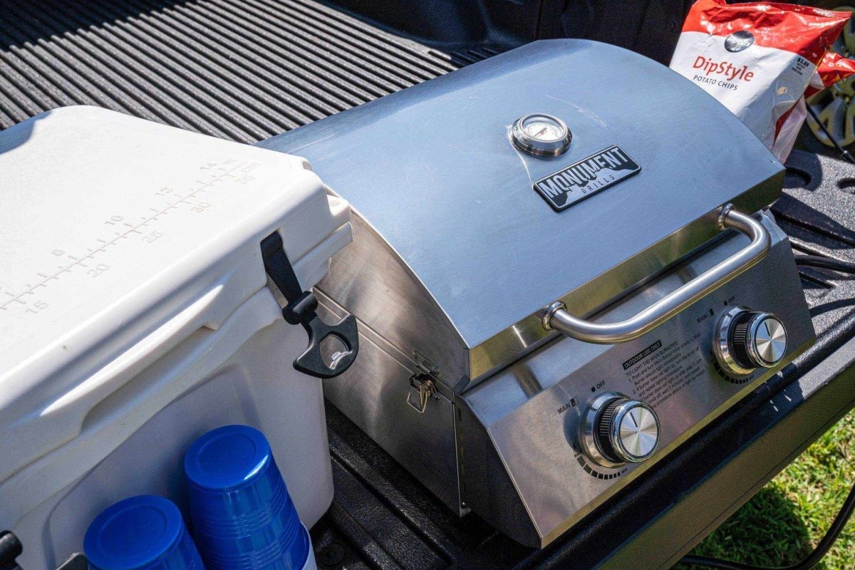 Propane grill on a truck bed with a cooler and blue cups nearby