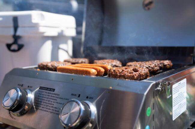 Grill with food cooking on it, showing knobs and brand name.
