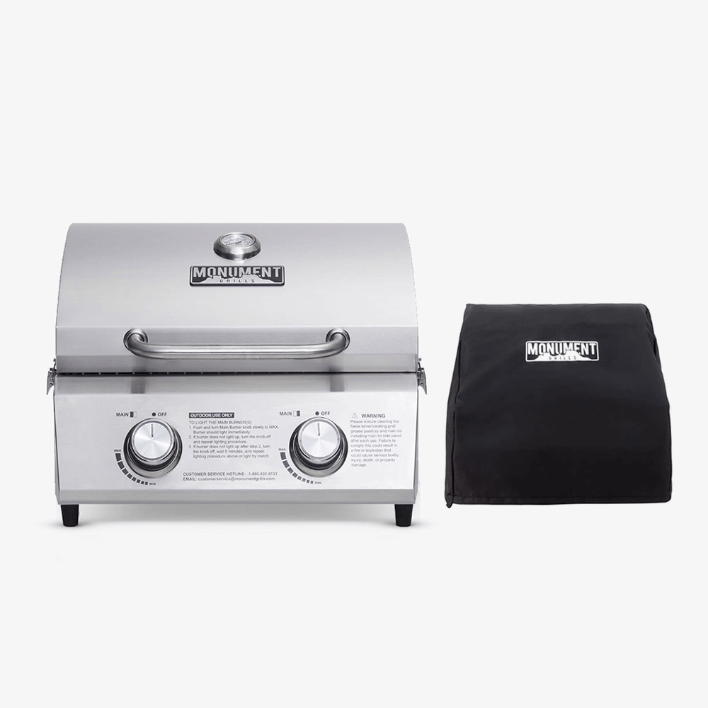A stainless steel outdoor gas grill with two control knobs, shown next to its black protective cover on a light gray background. The brand name 'MONUMENT' is visible on both the grill lid and the cover.