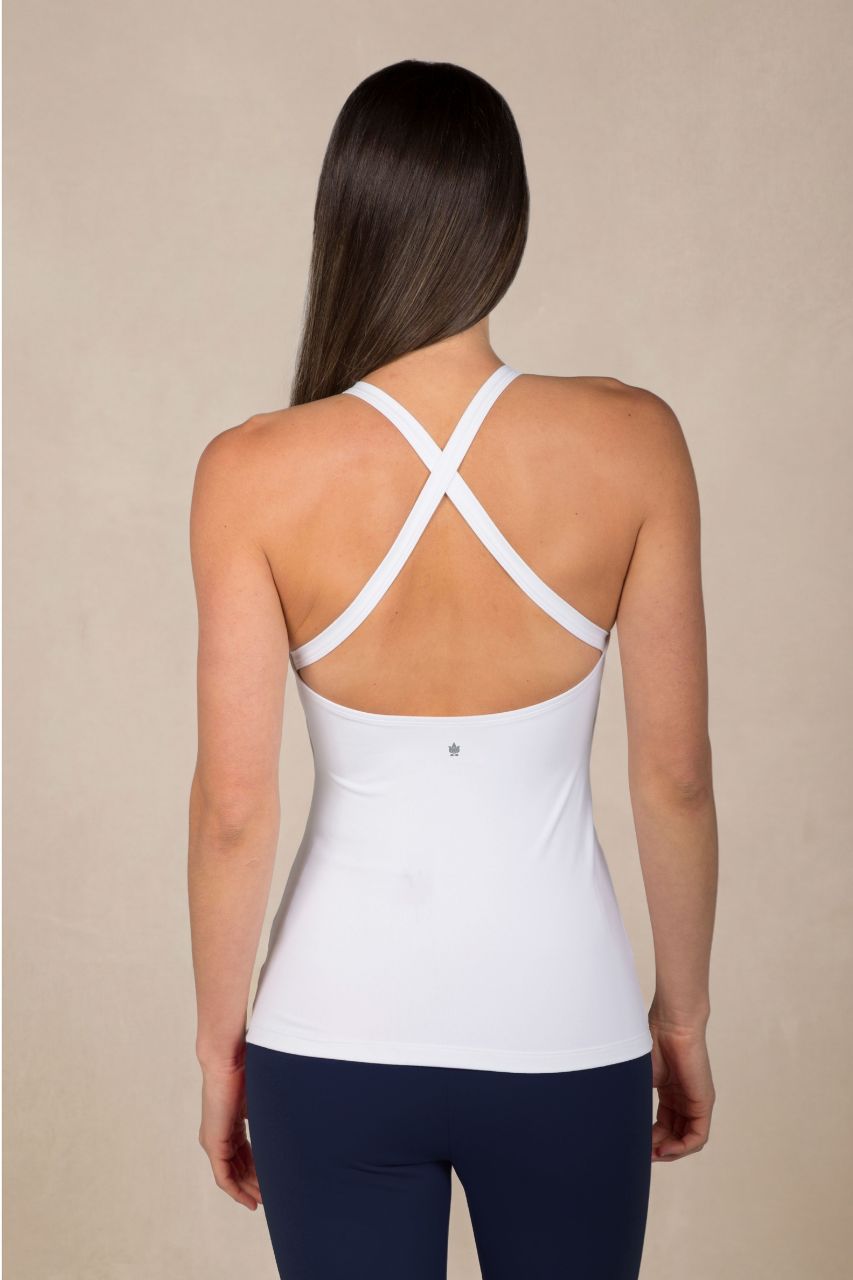 Woman wearing a white tank top with criss-cross straps on a beige background