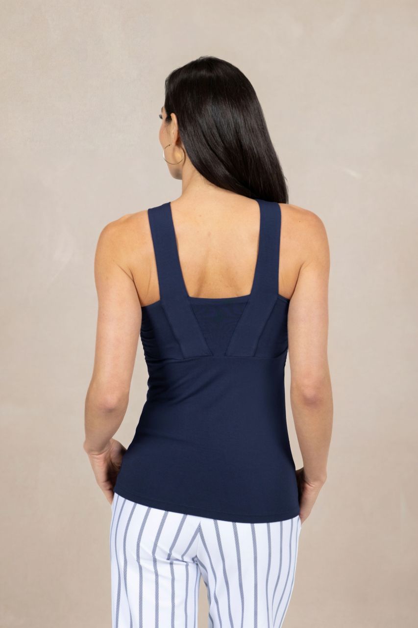 Woman wearing a navy tank top and white pants with black stripes on a beige background