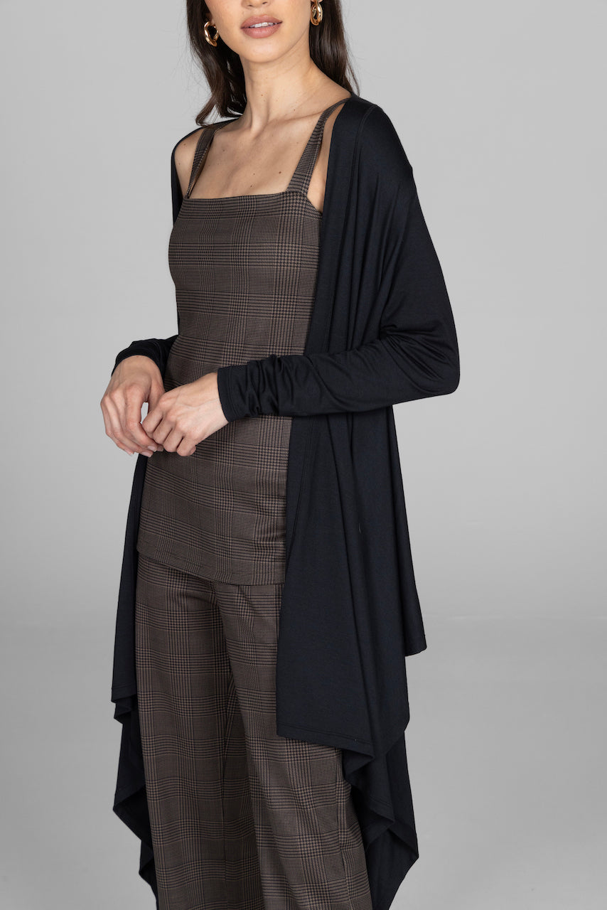 Woman wearing a black cardigan over a patterned dress on a gray background