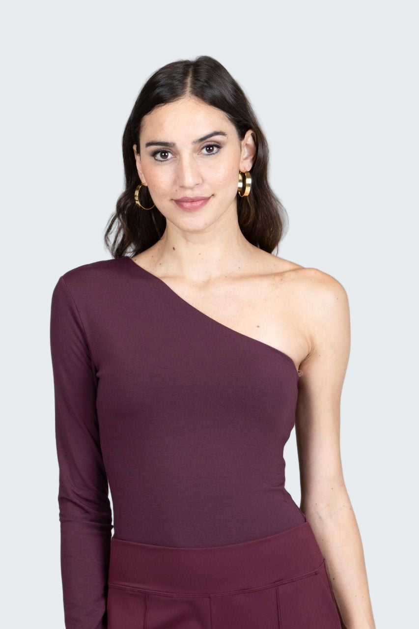 Woman wearing a one-shoulder purple dress against a gray background