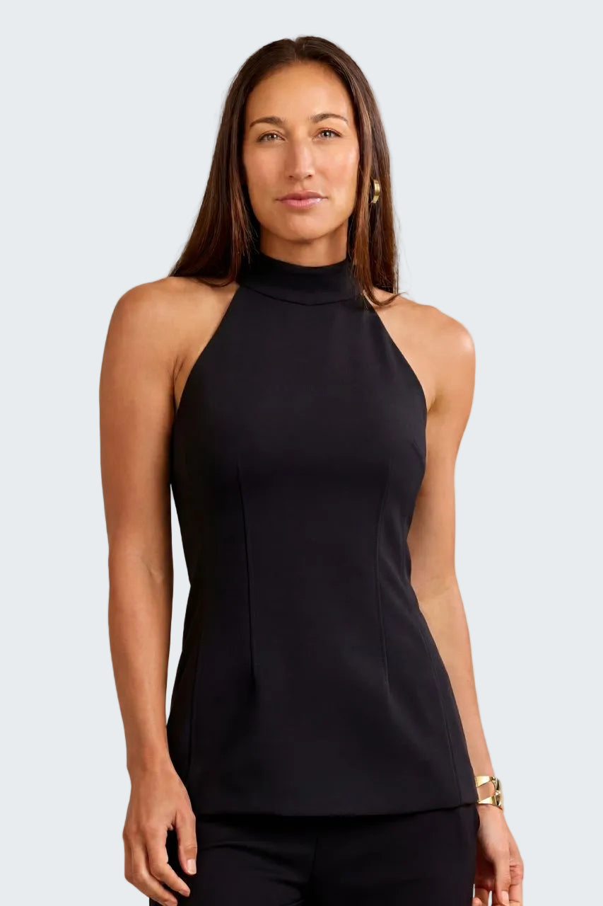 A woman modeling a sleeveless black mock neck top with structured side seams, paired with black pants, against a textured beige background.