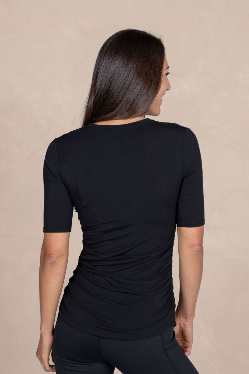 Woman wearing a black short-sleeve top and black pants against a beige background