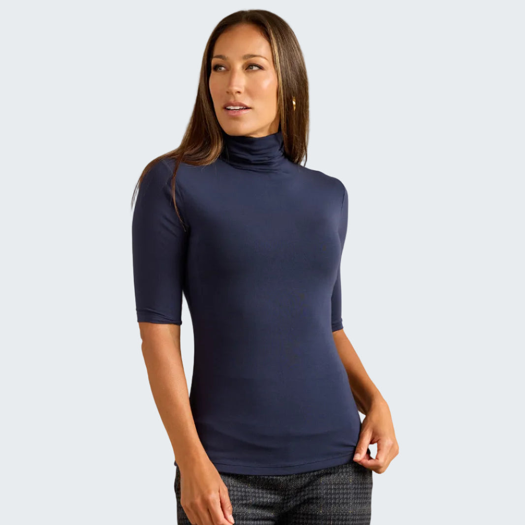 A woman modeling a navy blue short-sleeve mock neck top against a textured beige background.